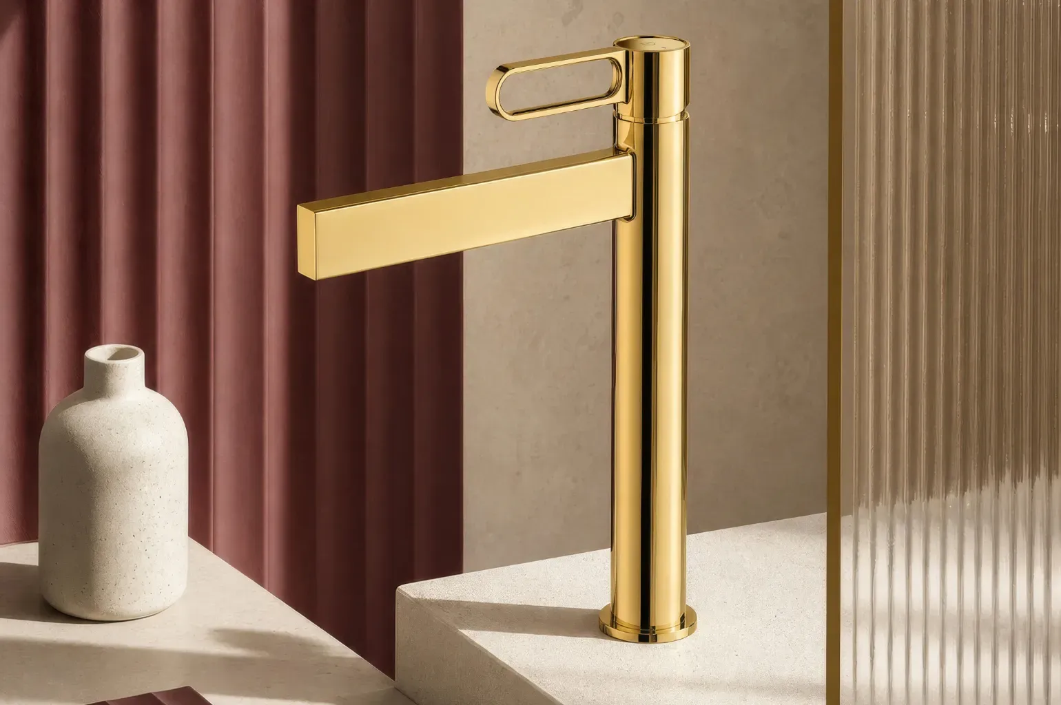Wysoka, nablatowa bateria umywalkowa ZAFFIRO w wykończeniu Gold zestawiona z ceramiką, trawertynem, kolorem bordo i ryflowanymi powierzchniami.